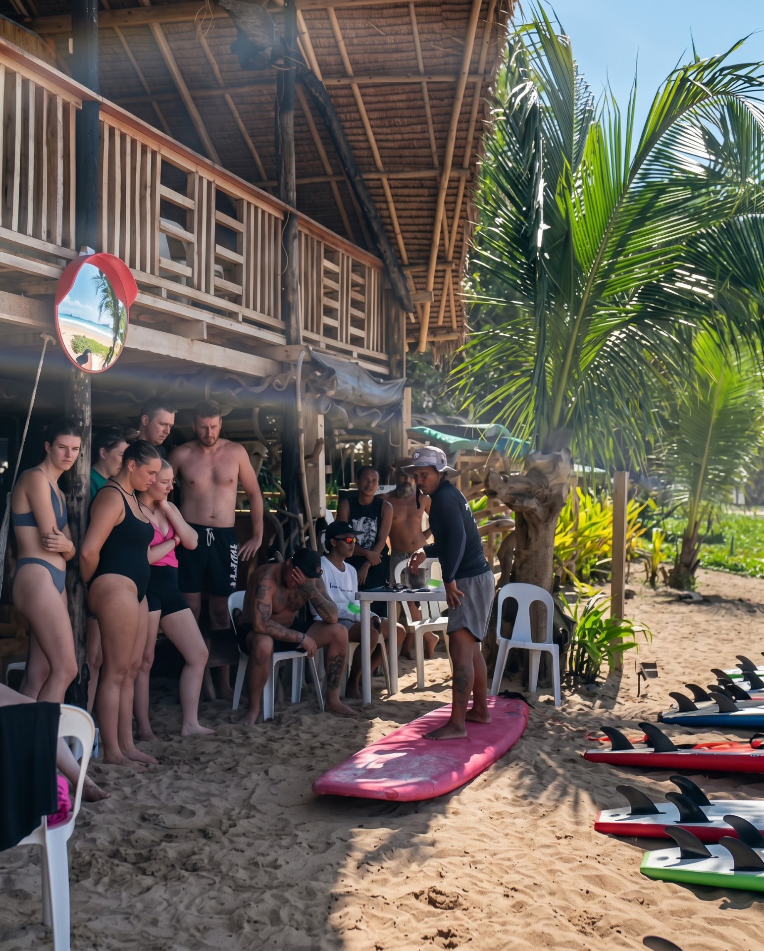 A surf instructor teaching ground school to a group under the beach hut at Duli Beach